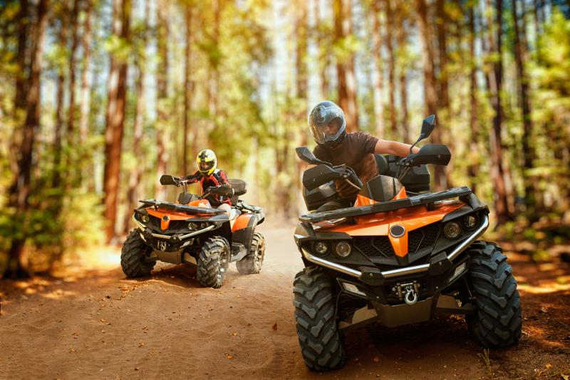 Photograph of two ATVs or four wheelers being ridden by people in safety gear in the forest