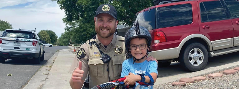 MCSO Deputy Pratt smiles and holds a thumbs up with a little boy and his bike.