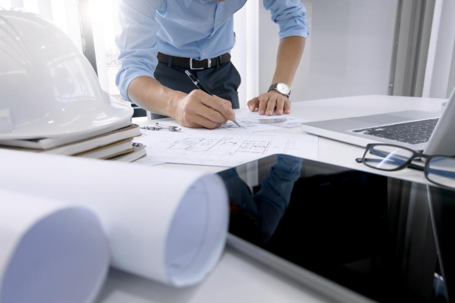 Photograph of Engineer working on blue prints on a desk with laptop