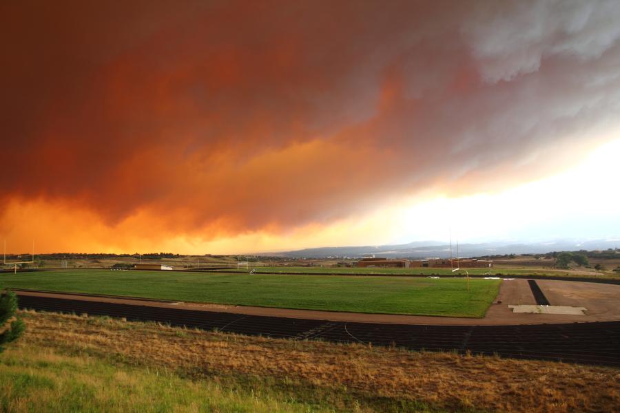 Photograph of Wildfire burning over valley with flames and large dark smoke cloud overhead