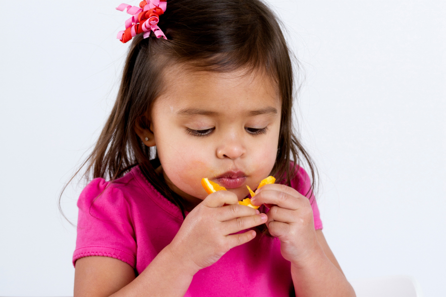 young girl with a bow in her hair eating a slice of orange