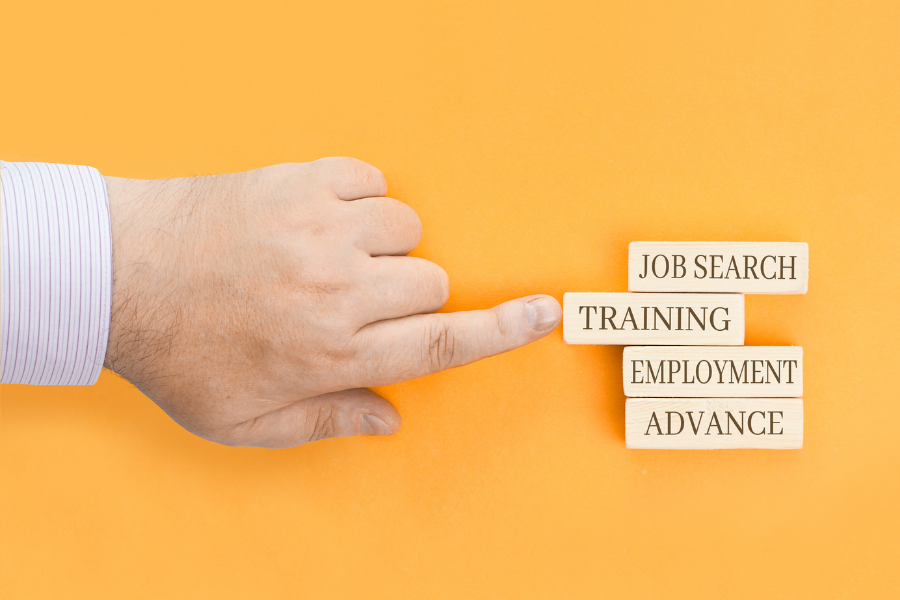 Yellow background with finger pointing at the word training on blocks with other words including job search, employment, and advance.