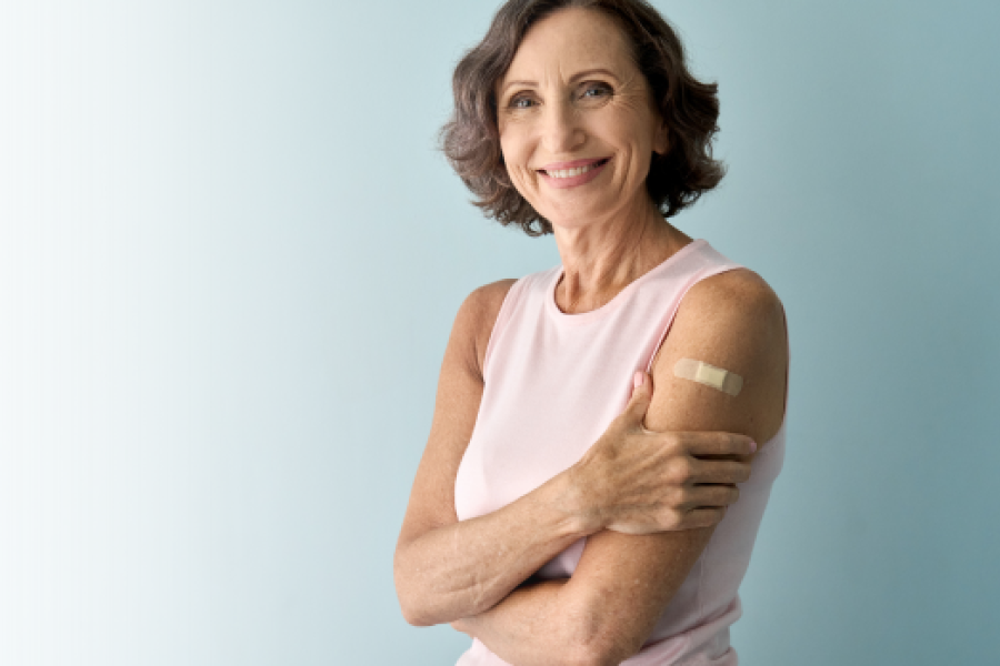 Smiling woman with short brown hair, who is wearing a pink tank top. She has a bandaid on her arm.