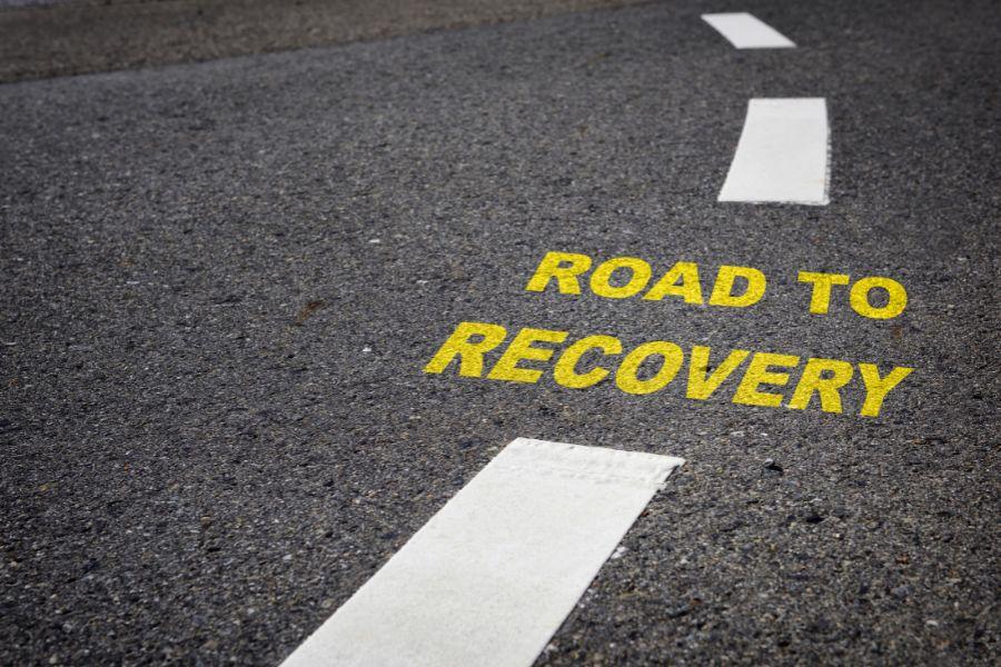 Road with white dashed lines in the middle and yellow text reading "road to recovery."