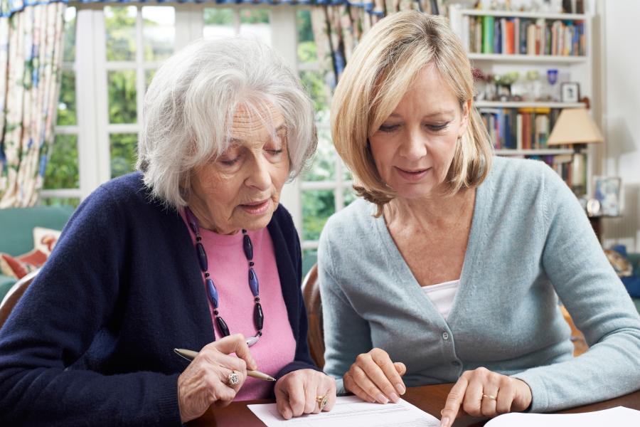 Photograph of female helps senior woman to complete form