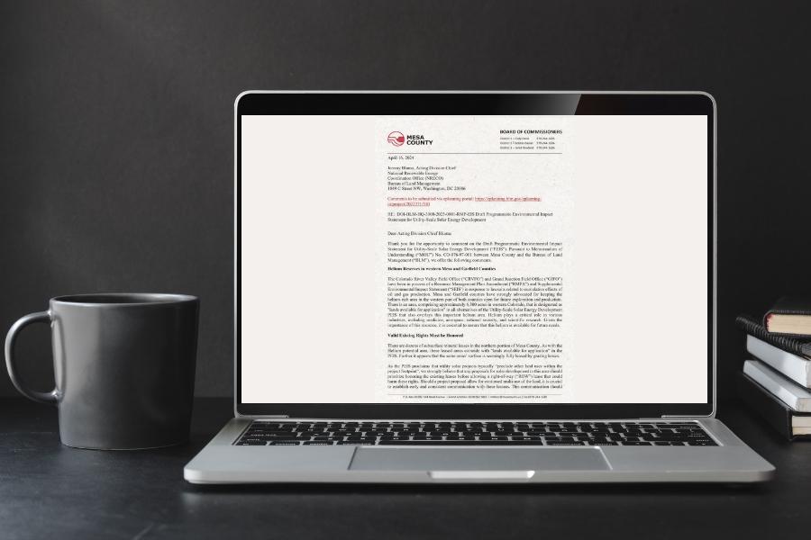 Laptop displays letter next to grey mug with grey background.