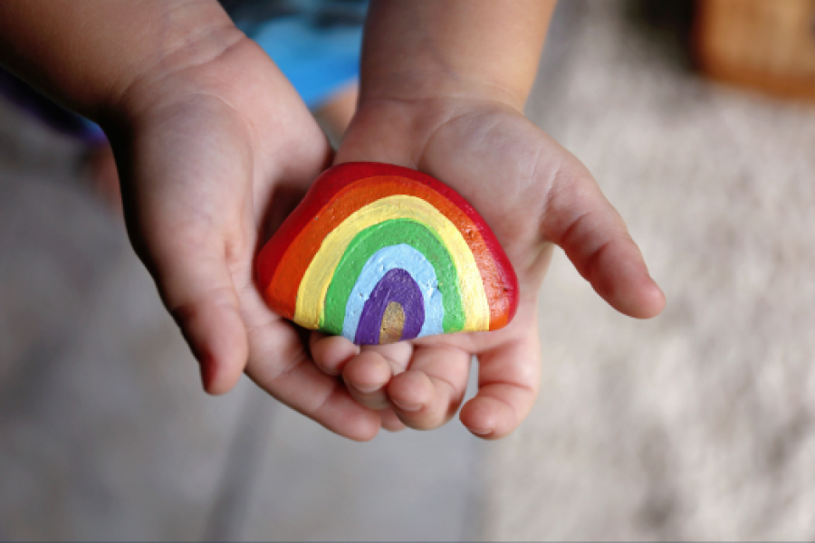 A closeup up a child's hands holding a rock with a painted rainbow on it.
