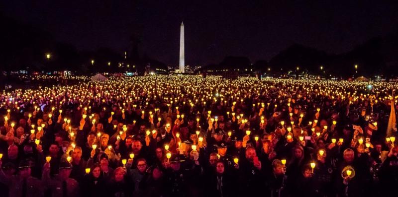 Photograph of Memorial Service in Washington DC with large group of people at night holding candles with Washing Monument in the background