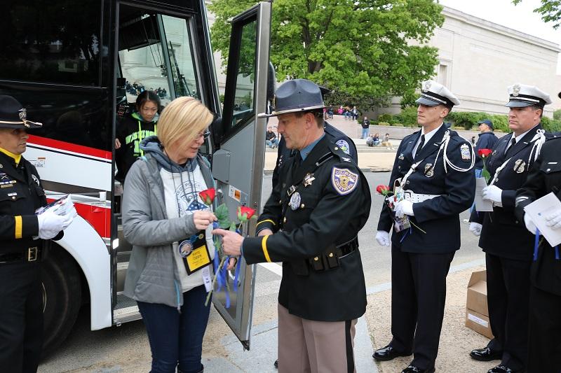 Photograph of woman receiving flowers from Colorado State Troopers in front of bus while visiting National Law Enforcement Monument 