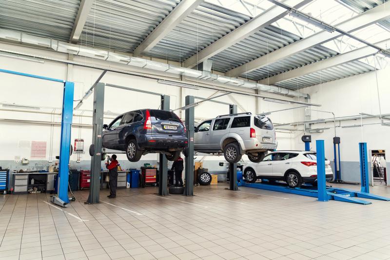 Photograph of the inside of an Auto Shop garage with three vehicles on lifts, two vehicle lifted up, employees working on the vehicles