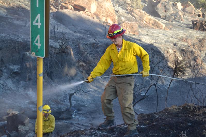 Photograph from Gibbler Gulch Fire of volunteer spraying water on hot spots on the side of the road