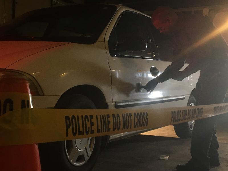 Photograph of a technician dusting a car for finger prints at a crime scene behind police line tape