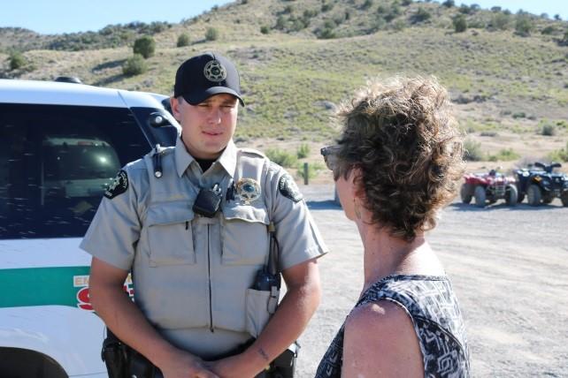 Photograph of a male patrol deputy speaking to a woman next to a Sheriff Vehicle in the desert with two four wheelers in the background