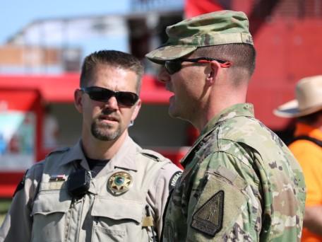 Photograph of a Sheriff Deputy speaking to a solider in fatigues or combat uniform