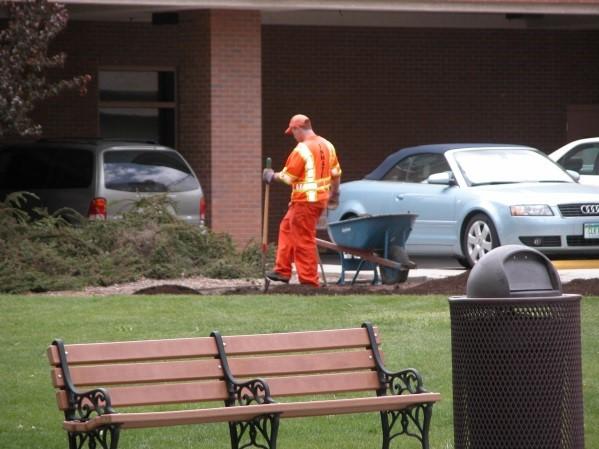 Photograph of an inmate during work opportunity program.  He is digging a hole with a wheelbarrow outside a building