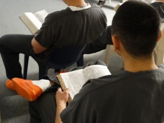 Photograph of inmates participating in Jail Ministry program.  Male inmate sitting in a chair holding a bible in lap