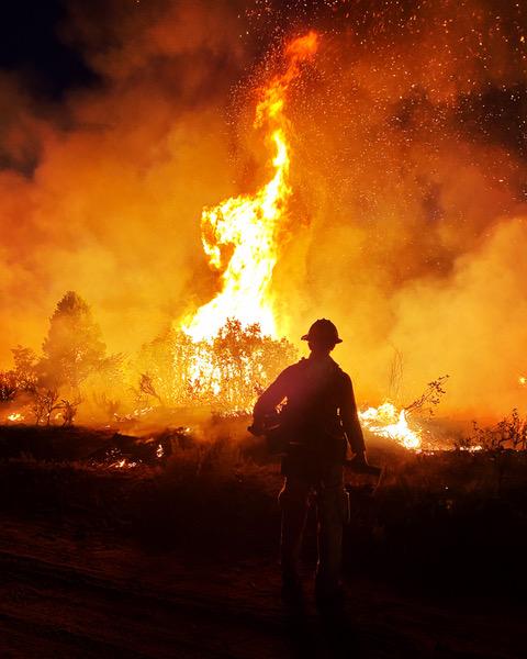 Photograph of Pine Gulch Fire. Fire Worker standing with Fire burning in the background