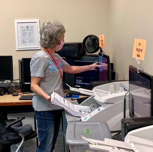 Photograph of a election volunteer feeding ballots into a tabulation machine