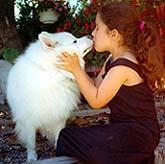 Photograph of a little girl kissing and receiving a kiss from her dog