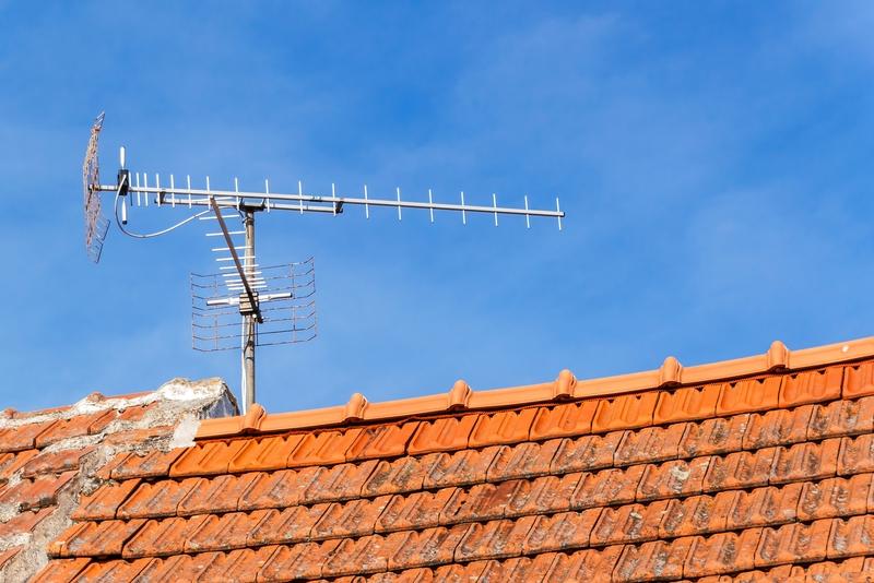 Photograph of an outdoor television antenna on the roof of a house with blue sky in the background