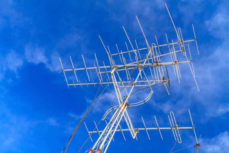 Photograph of an outdoor television antenna with blue sky and clouds in the background