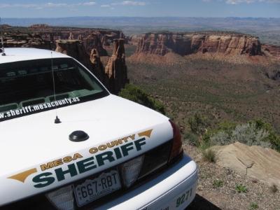 Photograph of a Mesa County Sheriff vehicle parked on a dirt road with the Colorado National Monument in the background