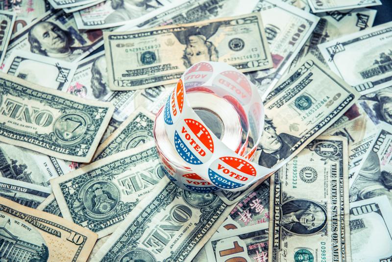 Photograph of a roll of "I Voted Today" sticker on a pile of money (One, Twenty, and 100 dollar bills)