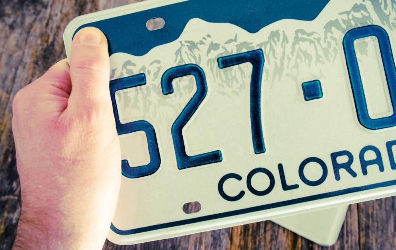 Photograph of Colorado License Plate held in hand with a desk in the background