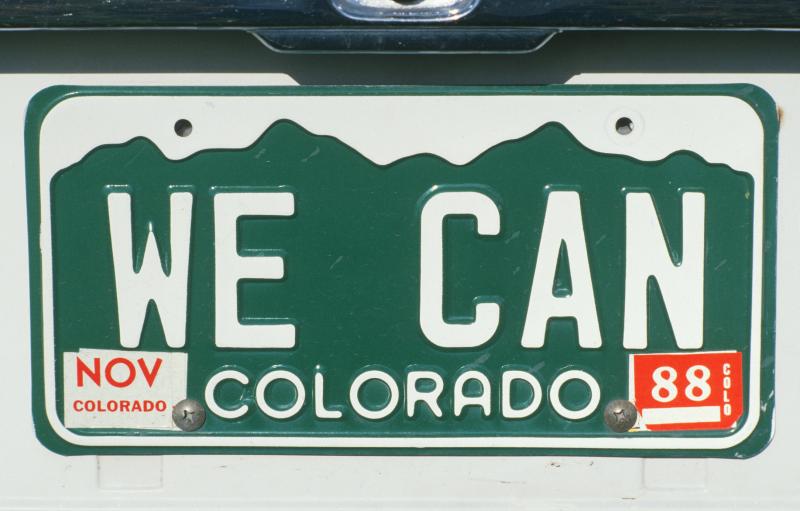 Photograph of Personalized Colorado License Plate with "We Can" printed on it, bottom right corner has NOV Colorado month sticker, and bottom right corner has 88 COLO year sticker