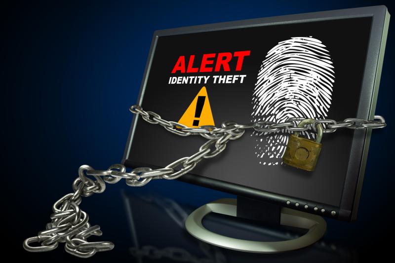 Photograph of Computer monitor with Alert Identity Theft, yellow triangle with! in the center, and chain with lock wrapped around the monitor