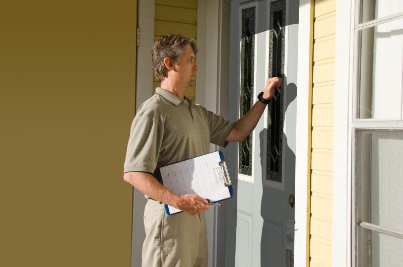 Photograph of a man knocking on the front door of a house with a clipboard  and pen in his hand.  Page on clipboard has a Survey Questionnaire printed on it 