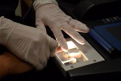 Photograph of technician with latex gloves using finger print machine to take prints