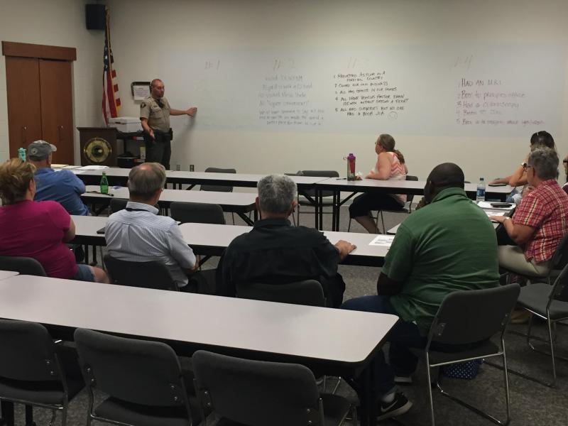 Photograph of a Mesa County Sheriff Deputy teaching a Victim Assistance Program class.  Deputy pointing at white board while talking to a group of people sitting around tables