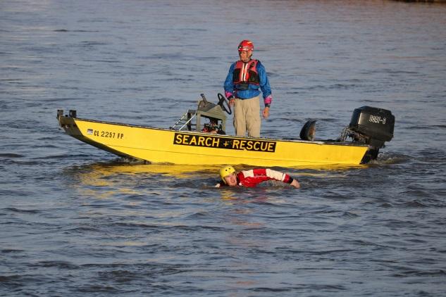 Photograph of Search and Rescue Team member in boat and another member swimming in water next to boat