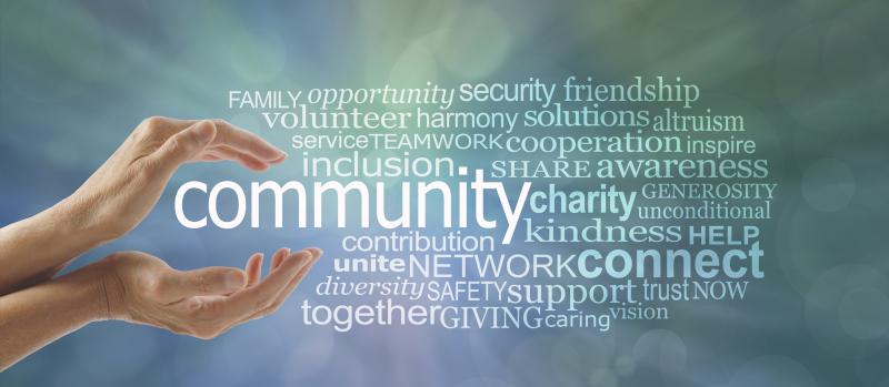 Concept Photograph of Community.  Female cupped hands around the word COMMUNITY and a relevant word tag cloud against a blue green bokeh background