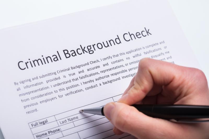 Photograph of Criminal Background Check form with a hand holding a pen over the form.