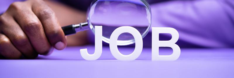 Concept photograph for job hunting.  Person s Hand Looking At Job Through Magnifying Glass On Desk