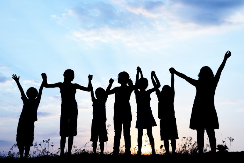 Silhouette of children of different heights holding hands up high at sunset.