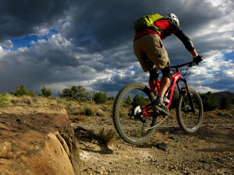 Rider jumping their bike off a ledge with a desert landscape and stormy sky.