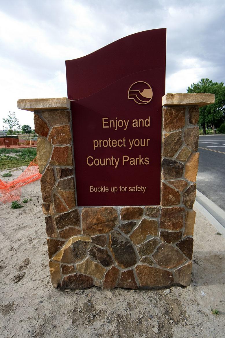 Maroon sign that says "Enjoy and protect your County Parks: buckle up for safety" on a flagstone base