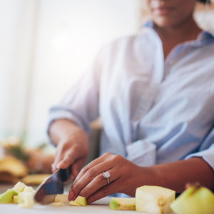 woman in long sleeved blue shirt chopping a green-yellow skinned apple