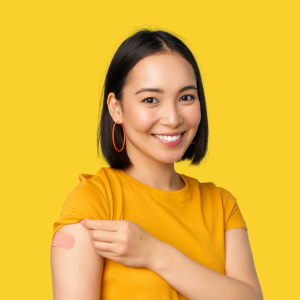 Woman wearing a dark yellow shirt showing a band aid on upper arm with a yellow background.