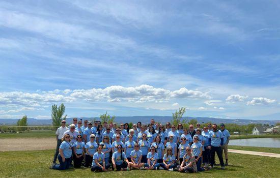 Staff photo outside with blue sky and green grass, employees all wearing similar t-shirts.