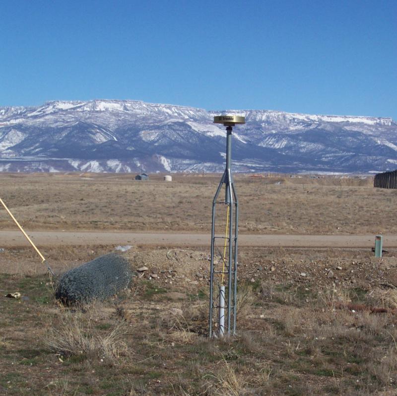 GPS choke ring antenna pushed into the the desert ground with a snow covered mountain in the background. 