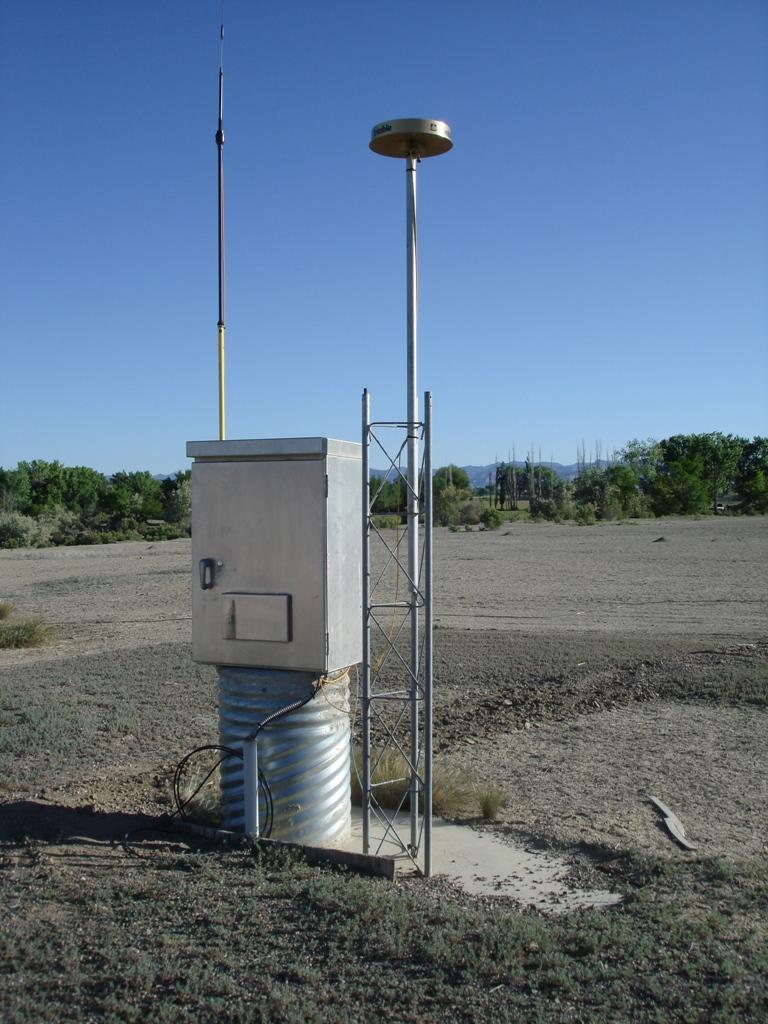 Antenna located in bare ground with green desert shrubs and brush located on the periphery. 