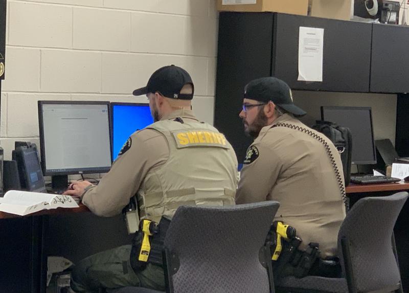 Two Mesa County Sheriff's Deputies sit facing a computer reviewing information.
