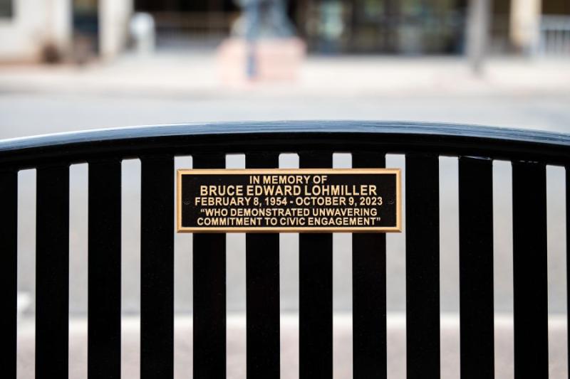 Close up view of black bench dedicated to community member with a gold plaque.