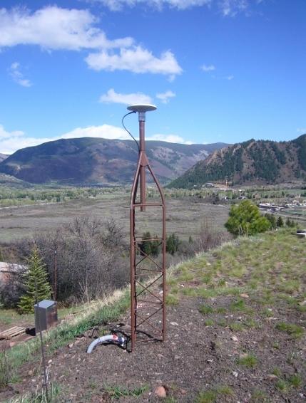 Antenna located on a grassy hillside looking over a mountain valley and mountains surrounding the valley. 
