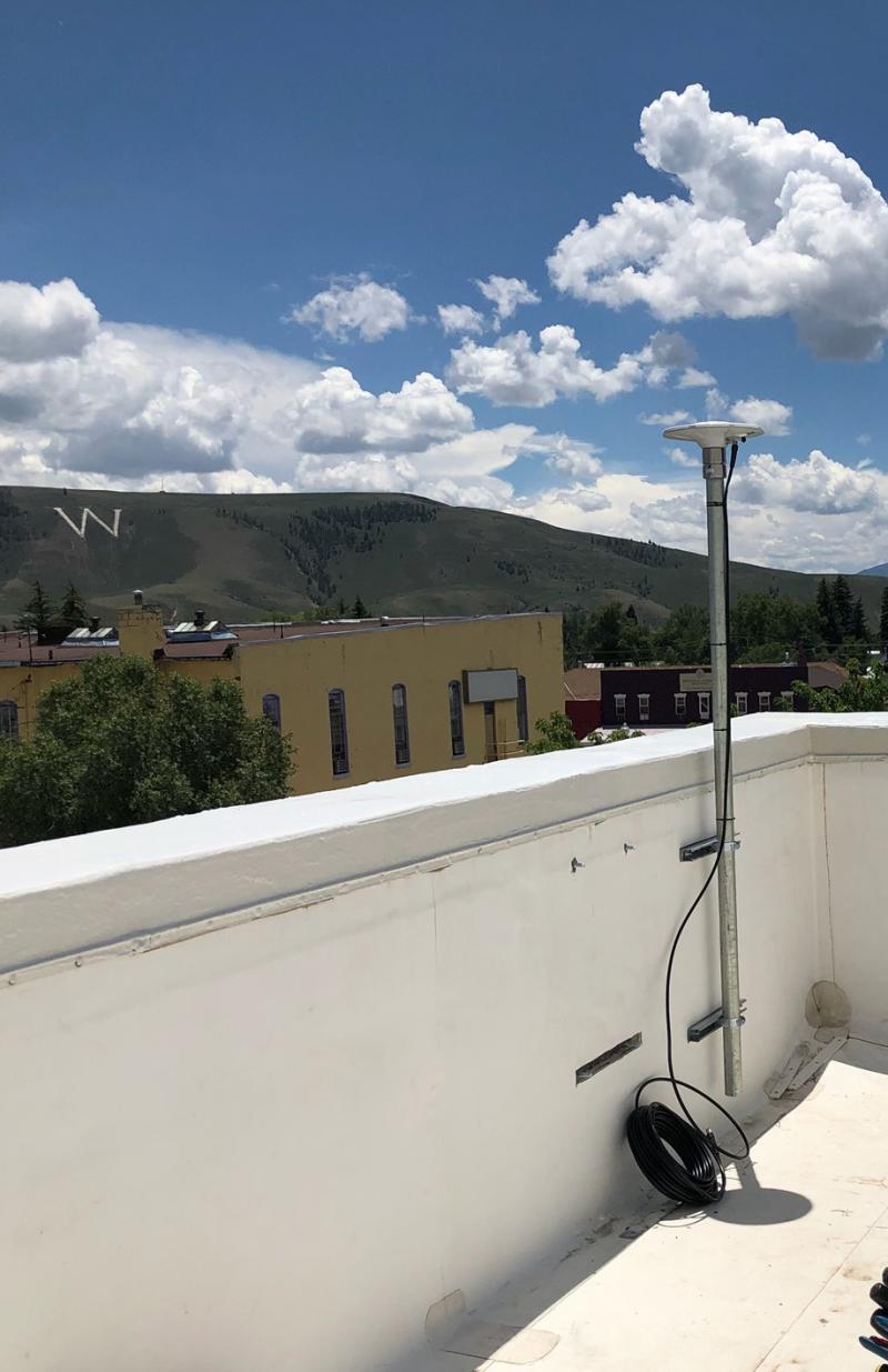 Antenna located on the white roof of multi-story building over-looking town and a mountain ridge with a large white W for Western State College.