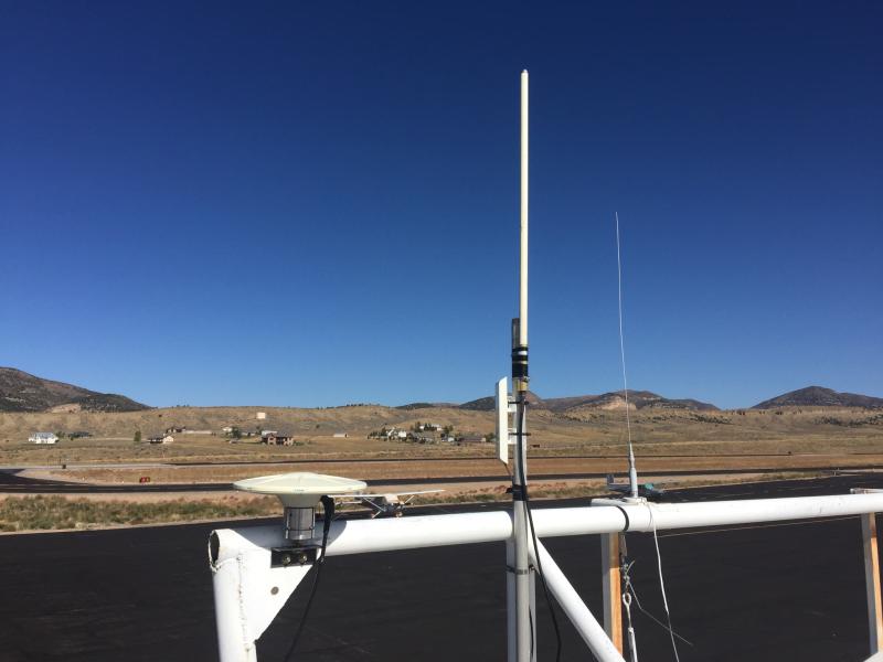 Antenna is situated on a white metal bar with several other antennae overlooking the airport runway.